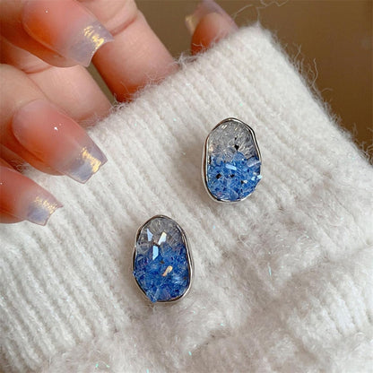 Glacier Blue Crystal Earrings on a textured white surface with a hand holding them.