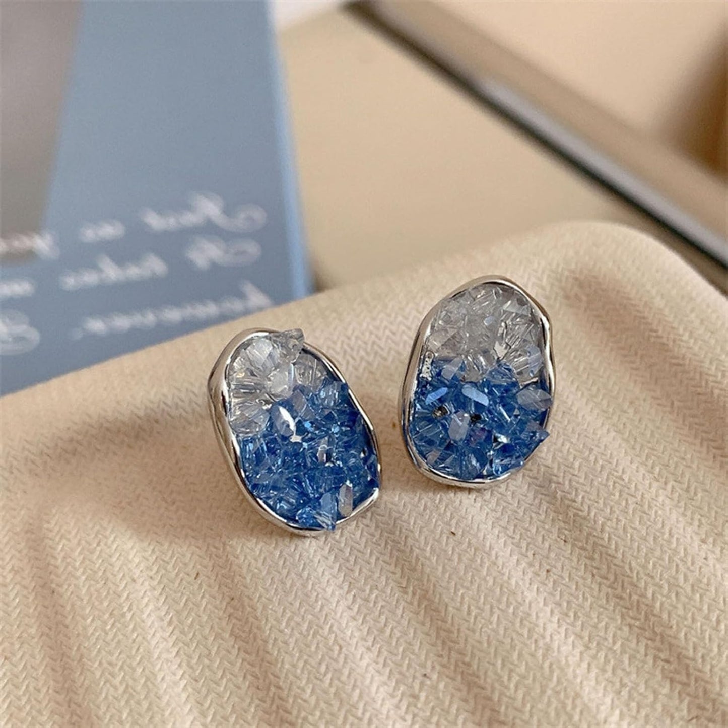 Glacier Blue Crystal Earrings on a beige surface with a blurred background