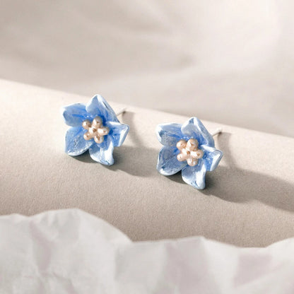 Pair of blue flower-shaped earrings with pearl centers on a beige surface.