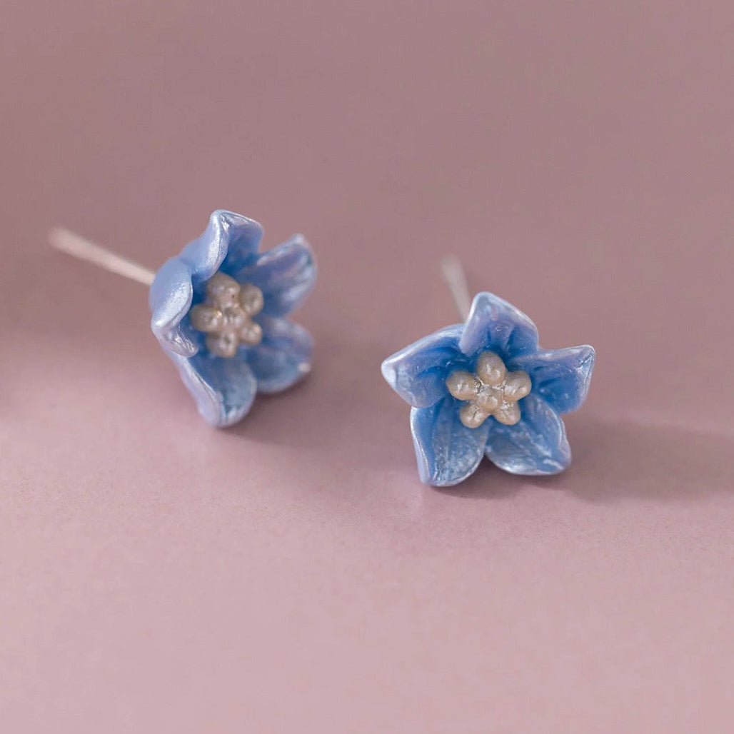 Pair of Blue Petal Blossom Earrings with pearl centers on a pink background