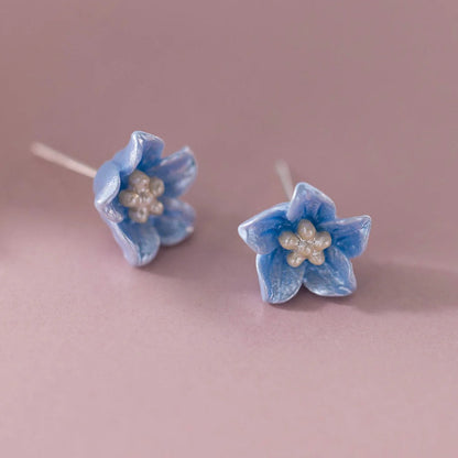 Pair of Blue Petal Blossom Earrings with pearl centers on a pink background